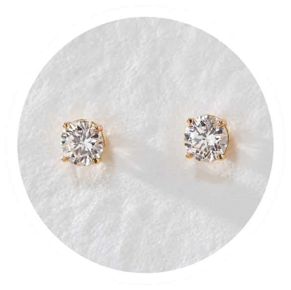 A pair of lab-grown diamond stud earrings on cream fabric